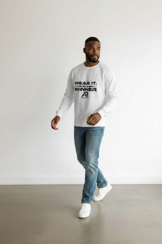 A man wearing a round neck sweater with the text 'WEAR IT, WINNER' walking in jeans and sneakers.