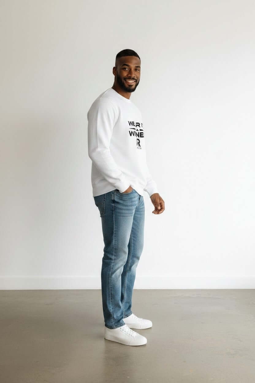 Man wearing a round neck sweater and jeans, smiling against a minimalist background.